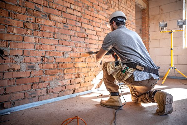 A builder works with a drill at a construction site. Handyman at a construction site in the process of drilling a wall with a perforator.